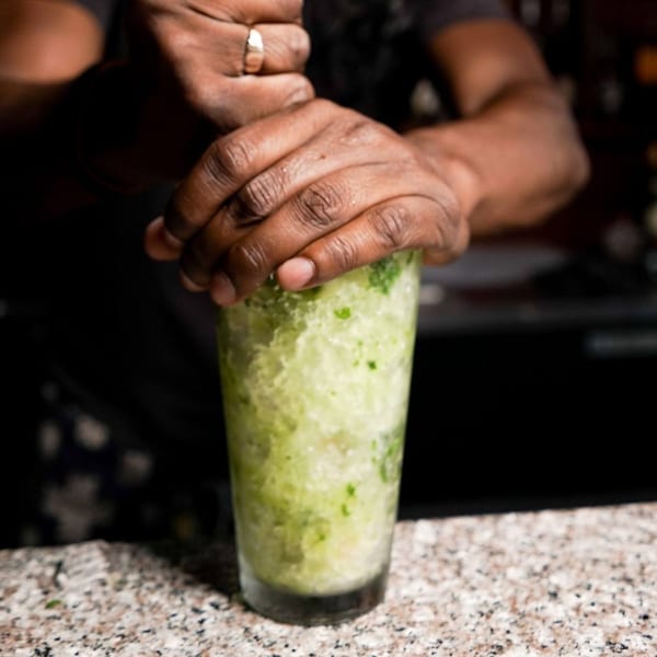 A bartender's hands muddling fresh mint and ice in a tall glass for a Caribbean cocktail.