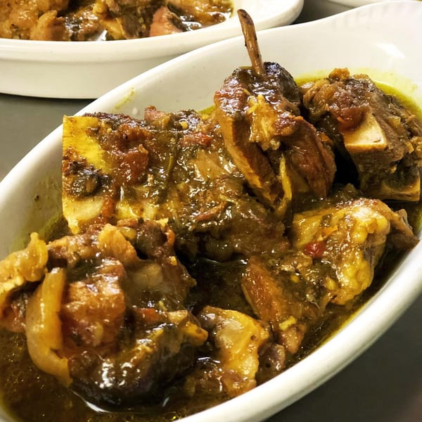 Close-up of Pam's Caribbean Kitchen's oxtail stew, rich brown meat and bones in a savory sauce.