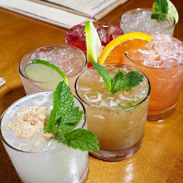 A vibrant array of six Caribbean cocktails, garnished with fresh mint, lime, and orange slices.