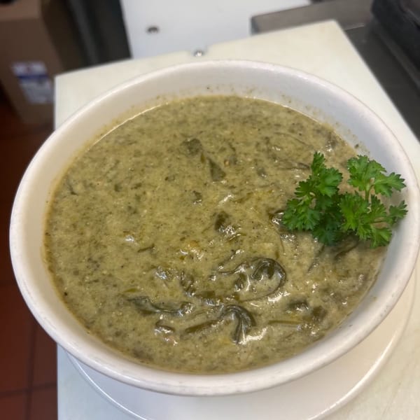 A white bowl of Pam's Caribbean Kitchen's callaloo soup, garnished with fresh parsley.