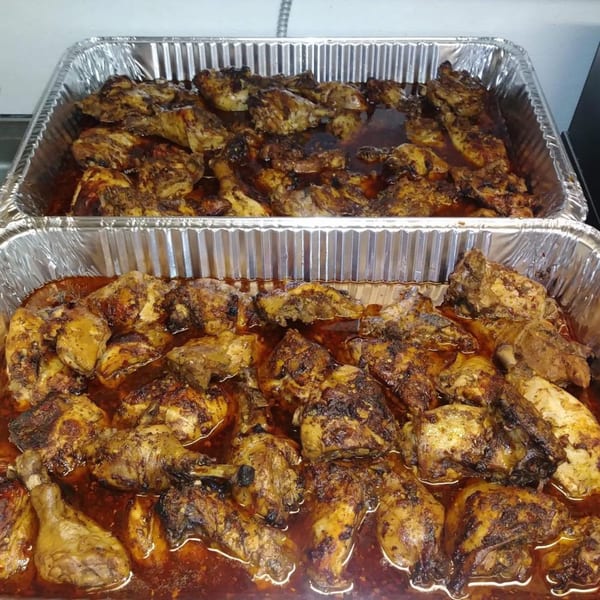 Two foil pans filled with Pam's Caribbean Kitchen's jerk chicken, glistening in sauce.