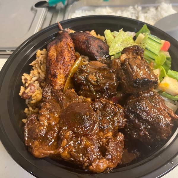 Pam's Caribbean Kitchen oxtail stew with rice, plantains, and a side salad in a black bowl.