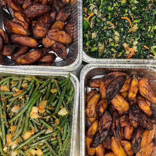 Four foil trays filled with Caribbean dishes: two with fried plantains, one with green beans, and one with greens.