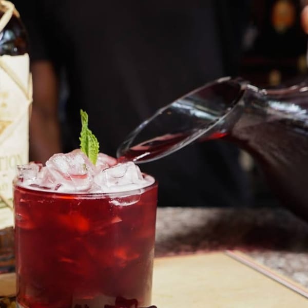 A Caribbean drink, garnished with mint, being poured into an ice-filled glass.